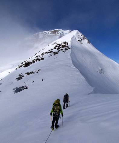 Hikers on the ridge of a snowy mounain with blue sky